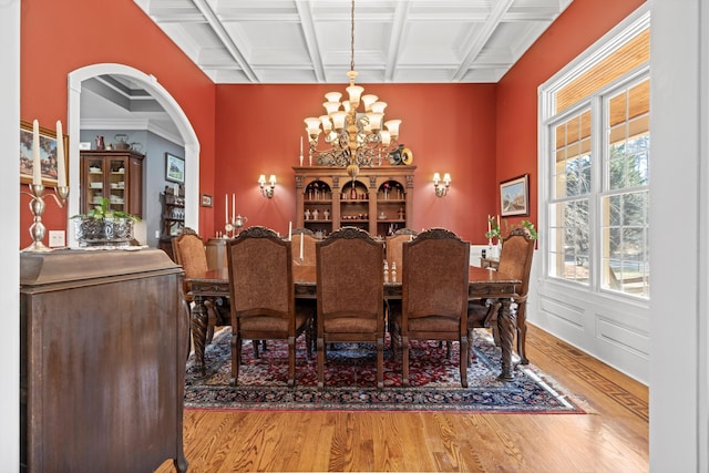 dining room with light wood finished floors, arched walkways, coffered ceiling, beamed ceiling, and a chandelier