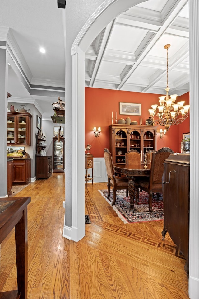 dining area featuring beam ceiling, light wood-style flooring, an inviting chandelier, ornamental molding, and coffered ceiling