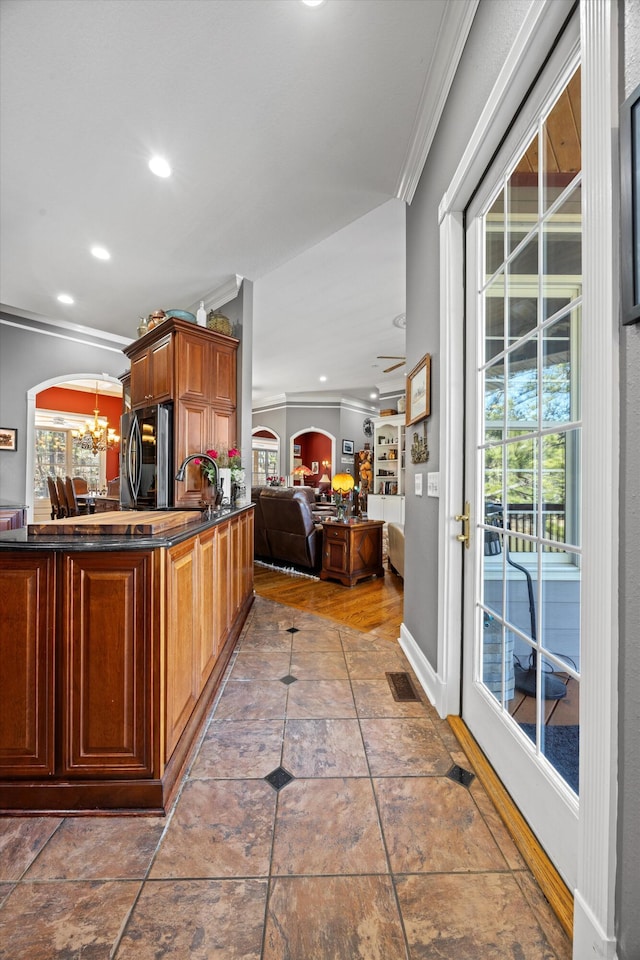 kitchen featuring arched walkways, crown molding, dark countertops, an inviting chandelier, and freestanding refrigerator