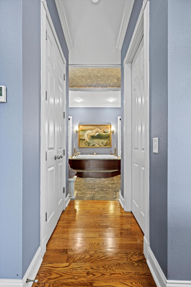 hall featuring a textured wall, crown molding, baseboards, and wood finished floors