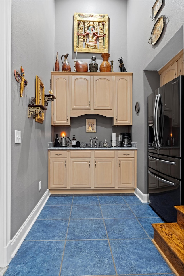 kitchen with dark tile patterned floors, black fridge, dark countertops, and light brown cabinets