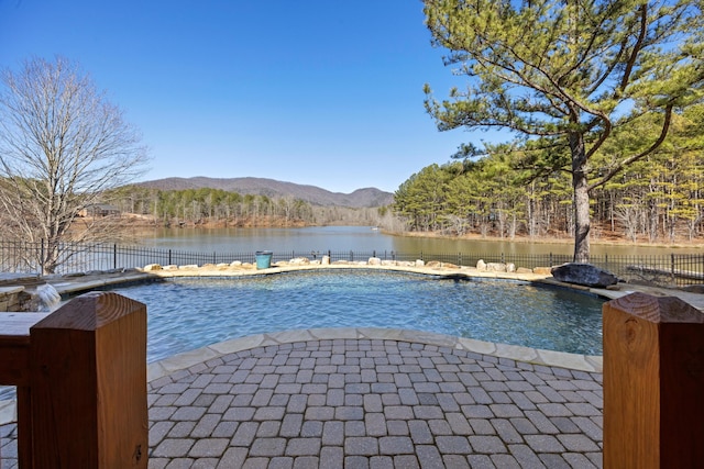 view of swimming pool with a wooded view, fence, a water and mountain view, and a fenced in pool