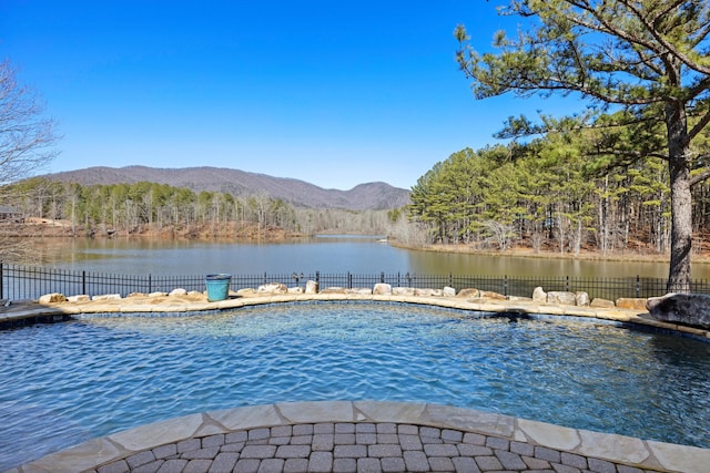 view of pool featuring a view of trees, fence, and a water and mountain view