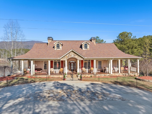 view of front of house featuring a fenced front yard, covered porch, a shingled roof, and concrete driveway