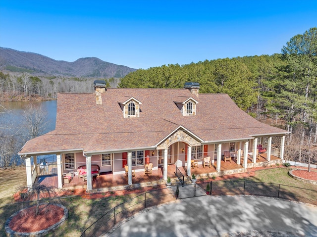 farmhouse-style home with fence private yard, a mountain view, covered porch, stone siding, and a chimney