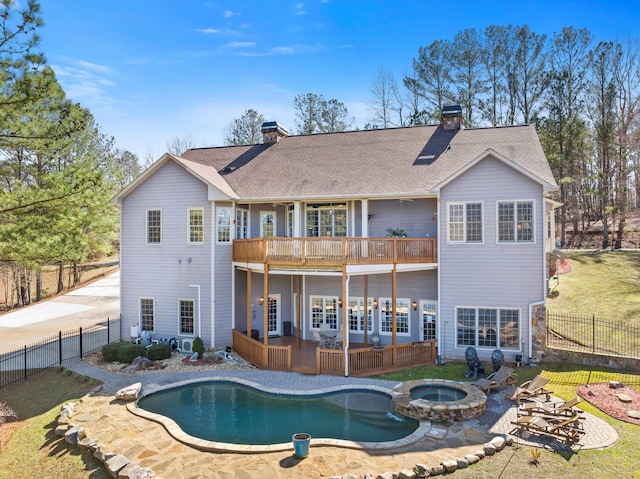 back of property with a shingled roof, a balcony, a fenced backyard, a chimney, and a pool with connected hot tub