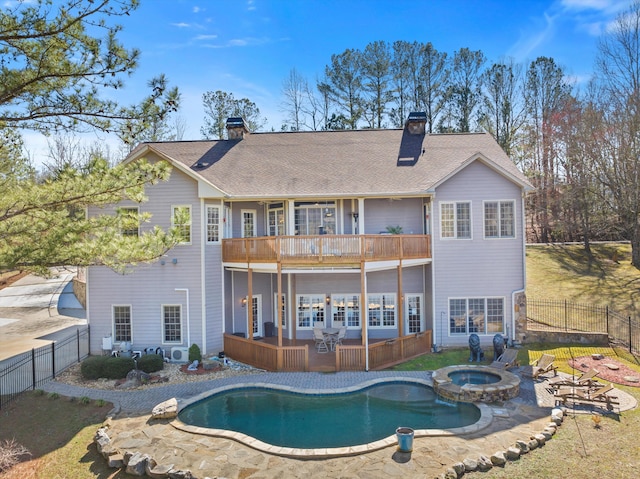 rear view of house with a balcony, a fenced backyard, a chimney, and a pool with connected hot tub