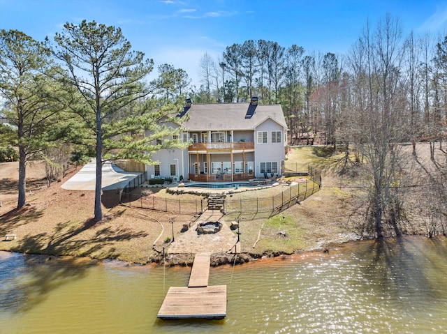 back of house with a chimney, a water view, fence, and a balcony