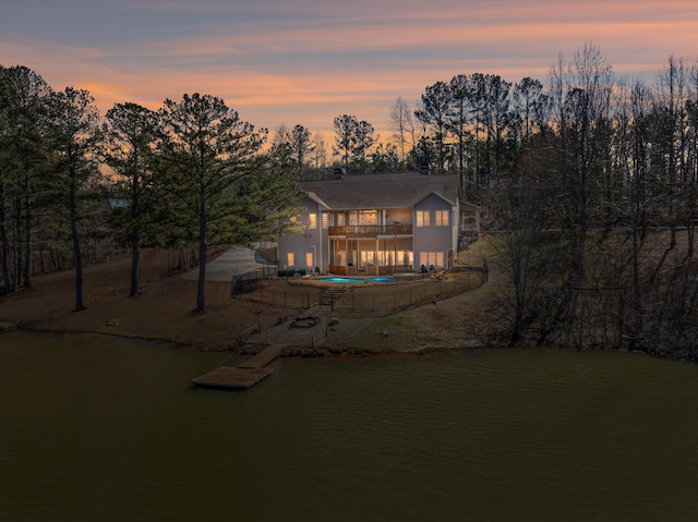 back of property at dusk with a water view and an outdoor pool