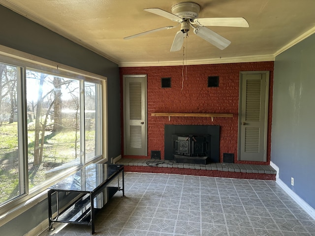 unfurnished sunroom featuring ceiling fan, a wood stove, and a healthy amount of sunlight