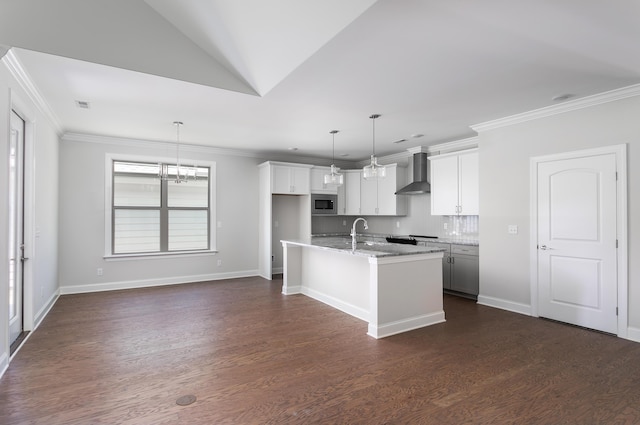 kitchen featuring pendant lighting, stainless steel microwave, light stone countertops, an island with sink, and wall chimney exhaust hood