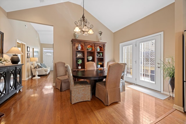 dining area featuring a chandelier, high vaulted ceiling, light wood-style flooring, and baseboards