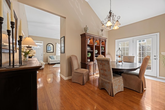 dining area with a chandelier, high vaulted ceiling, wood finished floors, and baseboards