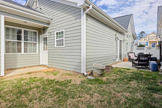 view of property exterior with roof with shingles, fence, a patio, and a yard