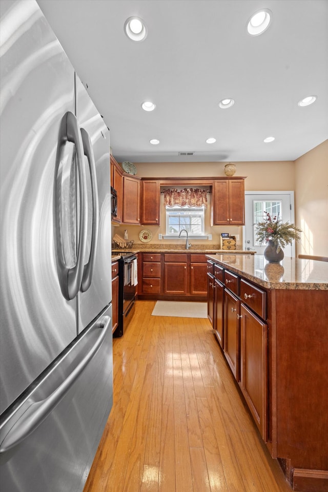 kitchen featuring black / electric stove, stone counters, a sink, light wood-style floors, and freestanding refrigerator