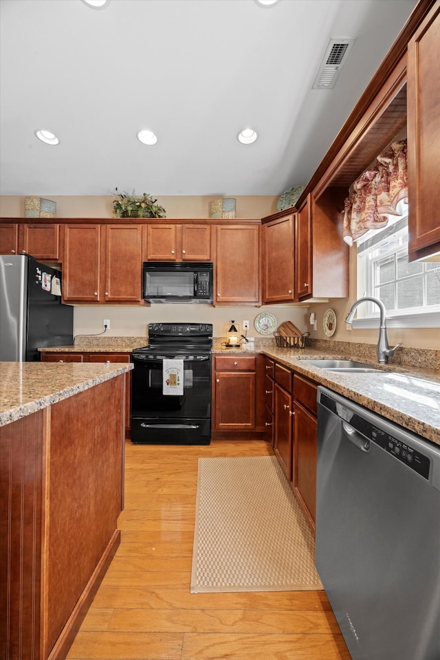 kitchen with light stone counters, light wood finished floors, visible vents, a sink, and black appliances