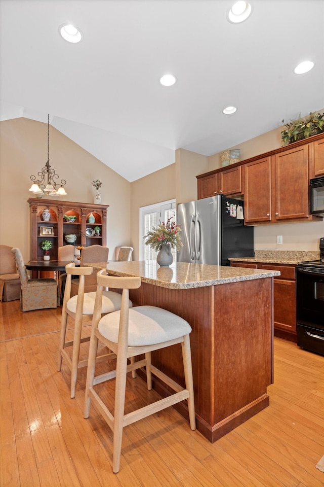 kitchen featuring brown cabinetry, light wood-style flooring, a breakfast bar, black appliances, and pendant lighting