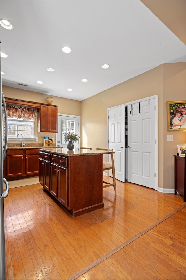 kitchen featuring recessed lighting, a center island, visible vents, light wood-style floors, and light stone countertops