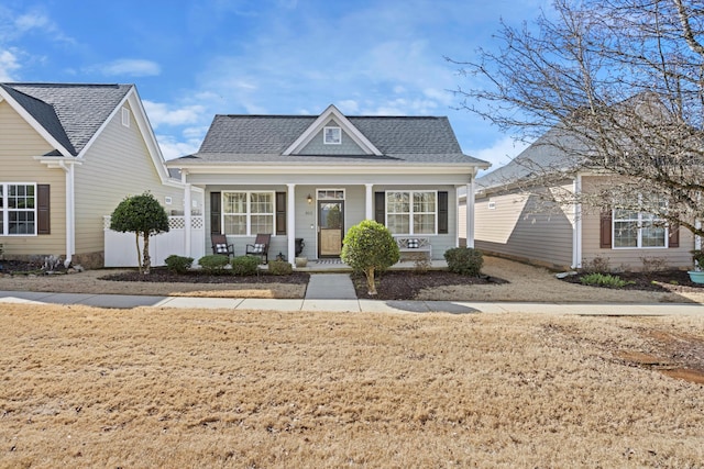 view of front of home with a porch, roof with shingles, and fence