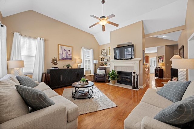 living area featuring baseboards, a ceiling fan, light wood-style flooring, a fireplace, and high vaulted ceiling