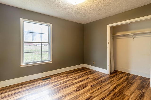 unfurnished bedroom with baseboards, visible vents, wood finished floors, a textured ceiling, and a closet