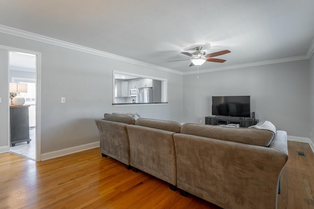 living area with visible vents, light wood-style floors, baseboards, and ornamental molding