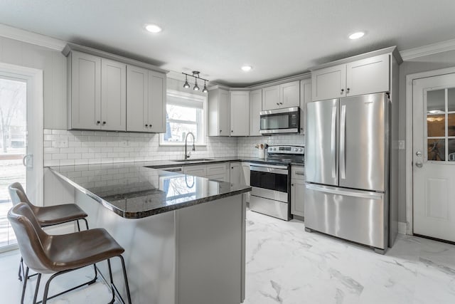 kitchen with ornamental molding, appliances with stainless steel finishes, a peninsula, and a sink