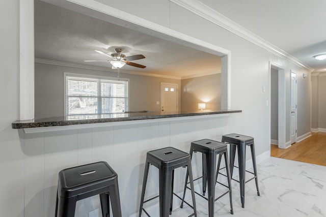 kitchen with a kitchen bar, marble finish floor, a ceiling fan, crown molding, and baseboards