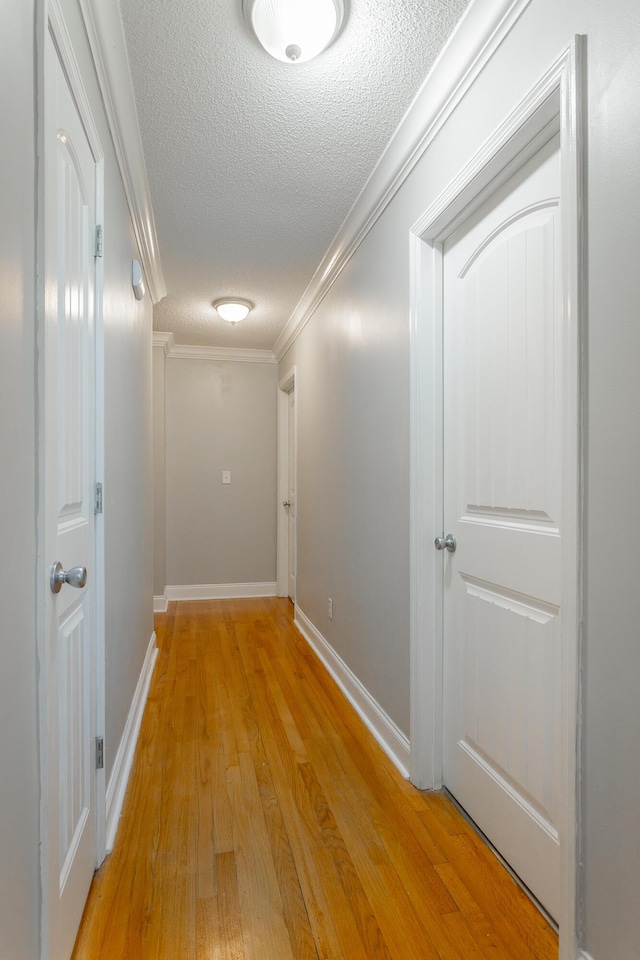 corridor featuring a textured ceiling, light wood-type flooring, crown molding, and baseboards