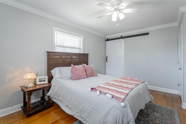 bedroom with a barn door, light wood-style floors, baseboards, and ornamental molding