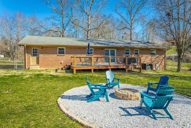 back of property featuring brick siding, a lawn, a fire pit, and a deck