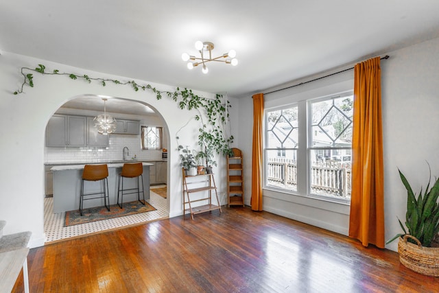 dining space featuring arched walkways, baseboards, dark wood finished floors, and a notable chandelier