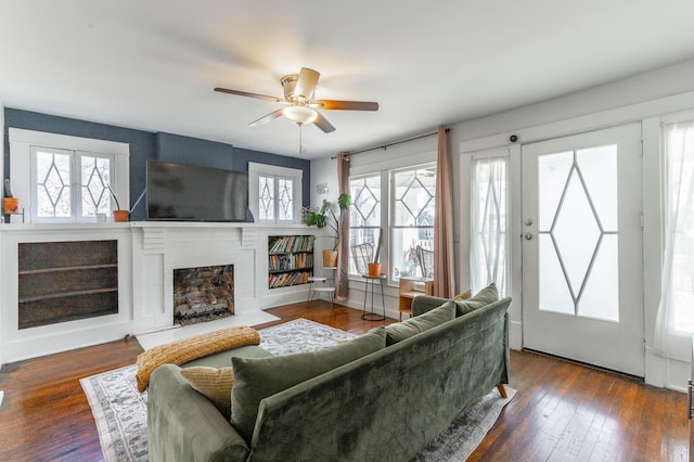 living area featuring dark wood-style flooring, a fireplace, a ceiling fan, and baseboards