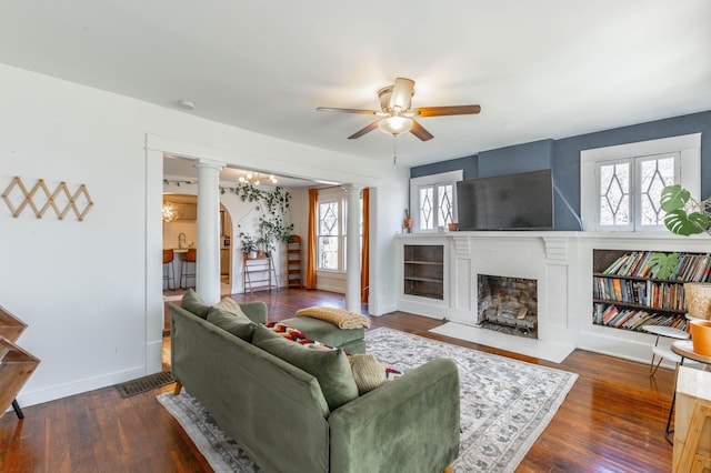 living room with ornate columns, a brick fireplace, baseboards, and dark wood-style flooring