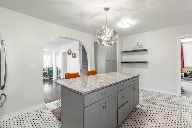 kitchen with arched walkways, hanging light fixtures, gray cabinets, light stone countertops, and open shelves