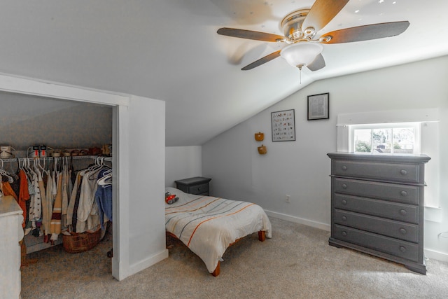 carpeted bedroom with a walk in closet, lofted ceiling, a closet, ceiling fan, and baseboards