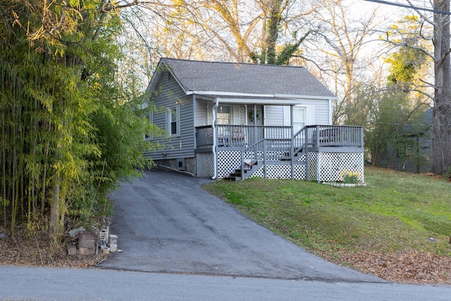 view of front of house with a front lawn, aphalt driveway, covered porch, and a shingled roof