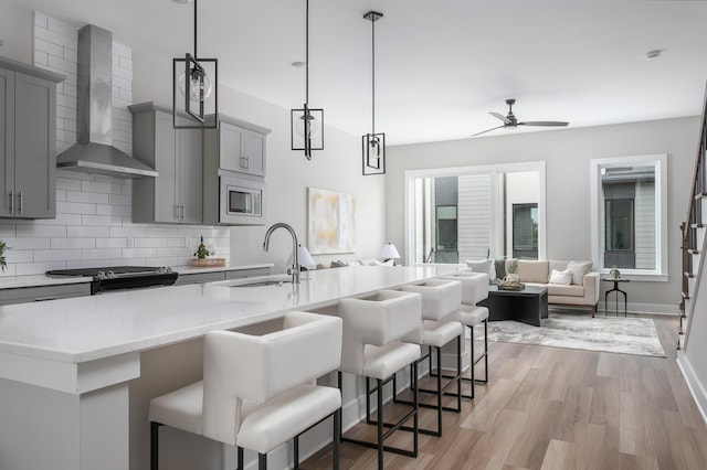 kitchen with wall chimney exhaust hood, sink, gray cabinetry, decorative light fixtures, and a kitchen breakfast bar