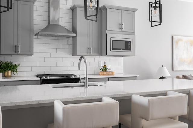 kitchen with gray cabinets, stainless steel microwave, sink, backsplash, and wall chimney exhaust hood