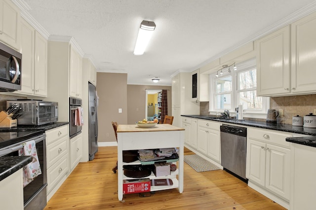 kitchen with sink, crown molding, light wood-type flooring, appliances with stainless steel finishes, and white cabinets