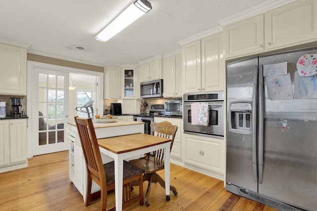 kitchen with stainless steel appliances, a textured ceiling, white cabinets, and light wood-type flooring