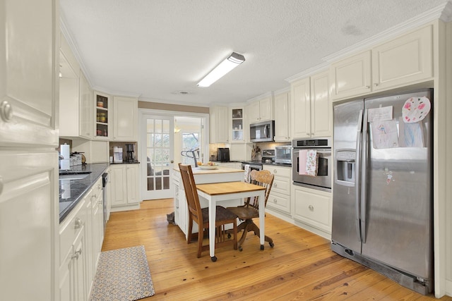 kitchen featuring light hardwood / wood-style flooring, appliances with stainless steel finishes, dark stone countertops, a textured ceiling, and white cabinets