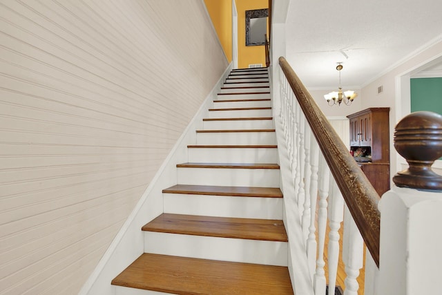 staircase with ornamental molding, a textured ceiling, and an inviting chandelier