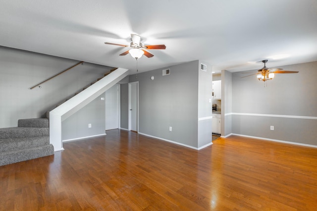 unfurnished living room with baseboards, ceiling fan, stairway, and wood finished floors