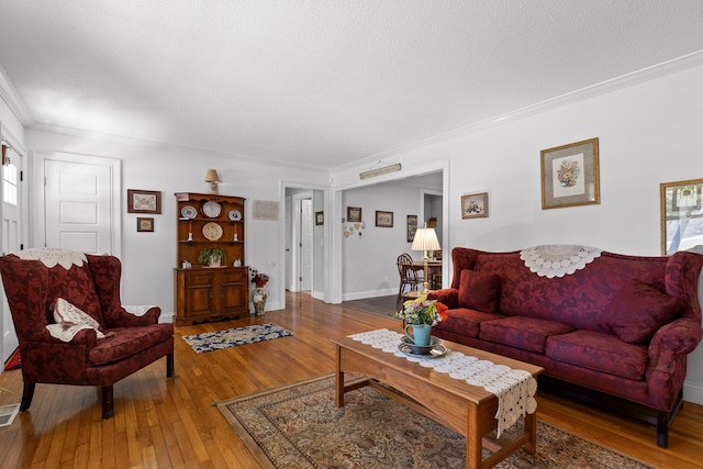 living room with baseboards, a textured ceiling, ornamental molding, and hardwood / wood-style floors