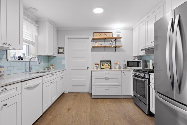 kitchen with light wood finished floors, white cabinets, appliances with stainless steel finishes, under cabinet range hood, and a sink