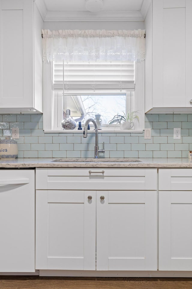 kitchen featuring white dishwasher, ornamental molding, white cabinets, and a sink