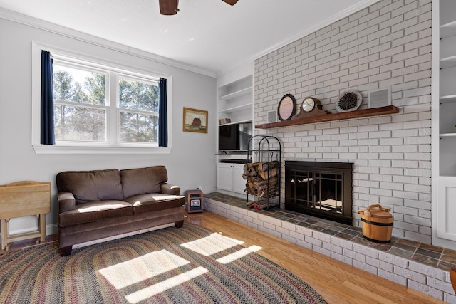 living room featuring built in features, a ceiling fan, ornamental molding, wood finished floors, and a fireplace