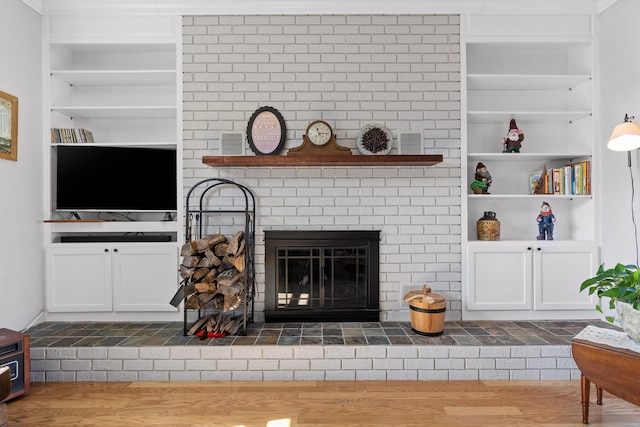 living area with built in shelves, a fireplace, and wood finished floors