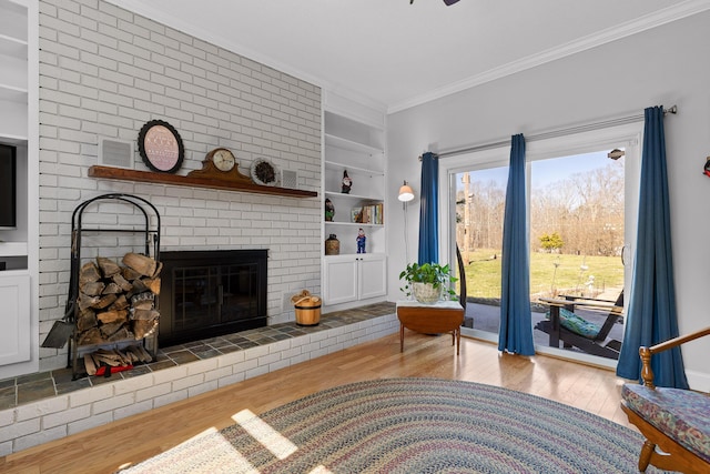 living room with built in features, visible vents, ornamental molding, a brick fireplace, and wood finished floors